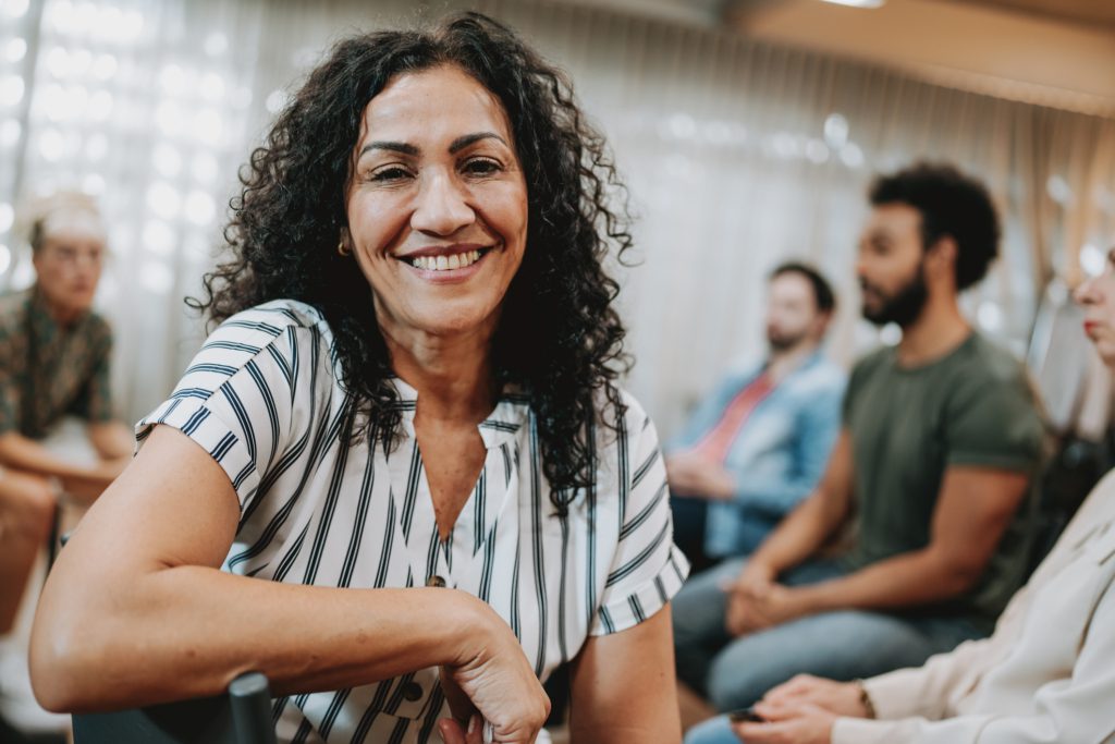 A woman in group therapy turns away from the group and smiles